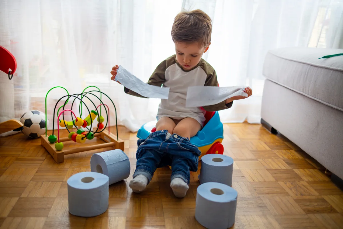 Toddler on a potty surrounded by toilet paper rolls